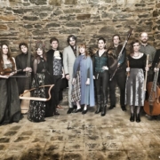 Makaris Celtic Band 12 musicians holding lyres, flutes, cellos standing against a stone wall